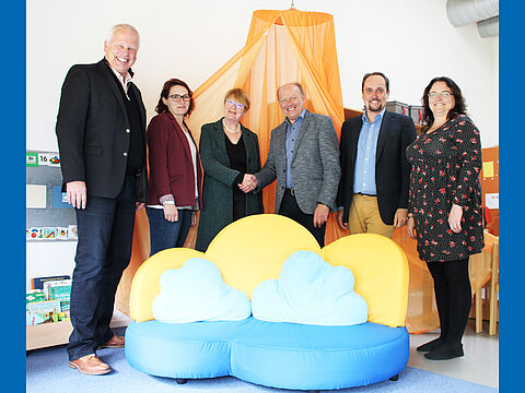 Vertreter der Lebenshilfe und der Firma omagaconsulting stehen hinter einer Couch für Kinder mit wolkenförmigen Kissen