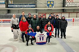 Personengruppe auf Eisfläche im Stadion, darunter Einshockeyspieler, Besucher und Kinder, die ein Vereinstricot halten